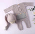 A baby knit outfit set laid flat on a pale pink background, including a long-sleeve footed romper in a textured light beige knit with a gray front patch and wooden buttons, plus a matching knit hat with a long tail and pom-pom. Decorative flowers appear at the edges.

Shopify Tags:
newborn outfit, baby romper, waffle knit romper, newborn romper, baby boy outfit, baby girl outfit, gender neutral baby, newborn coming home, coming home outfit, newborn photo outfit, baby photoshoot outfit, newborn photography, 