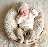 A sleeping newborn baby wearing a cream knit onesie with &