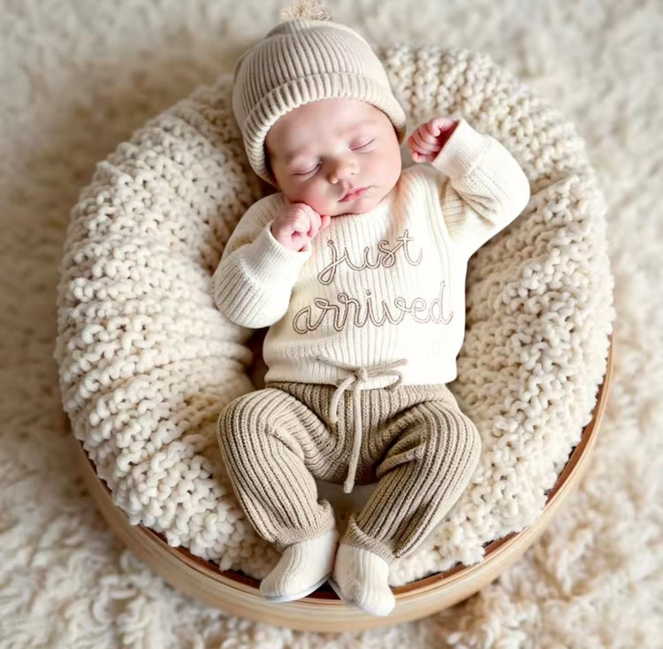 A sleeping newborn baby wearing a cream knit onesie with &