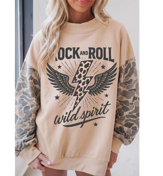 A woman wearing a beige crewneck sweatshirt with a graphic print of a lightning bolt over wings and the words &